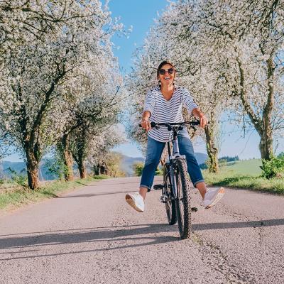 Happy smiling woman riding a bicycle under apple blossom trees.
