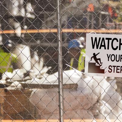 A 'watch your step' warning sign on the fence of a construction site.