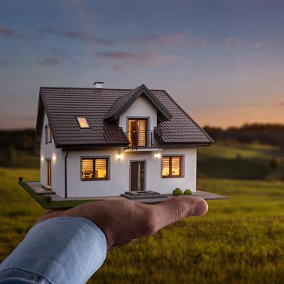 A figure of a house on a person's hand with a sunset background.