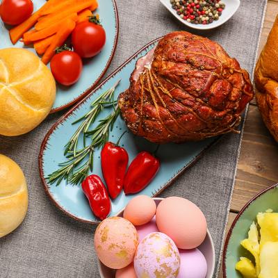 Easter dishes such as honey ham, baked buns, potatoes and colorful easter eggs on a wooden table.