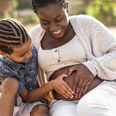 A black mother and her son touching her pregnant belly doing heart shape with hands.