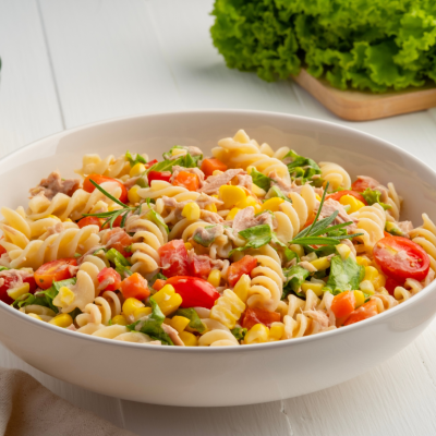 Homemade macaroni salad with trivelle pasta and canned tuna, carrot, lettuce, tomato, corn and mayonnaise dressing in a white plate on wooden table.