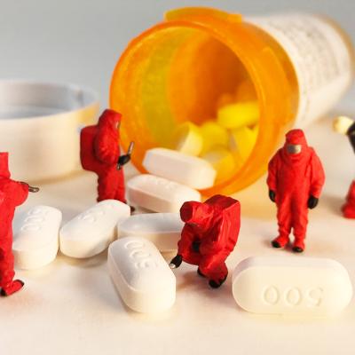Spilled opioid pills from the bottle and miniature first responders in biohazard suits are investigating it.