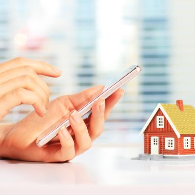 Person using smartphone and a figure of a house is on the same frame as a concept of paying rent digitally.