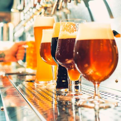 Different types of beer in unique glasses with bartender in background.
