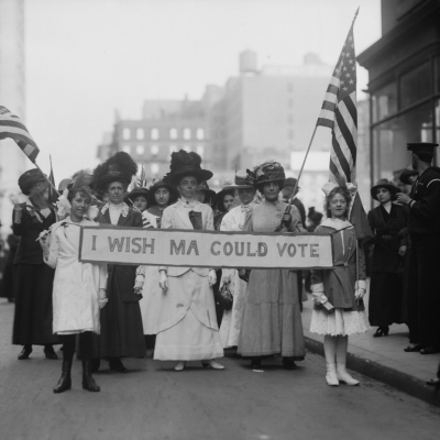 A group of Women's Suffrage activists march in a parade carrying a banner reading 'I Wish Ma Could Vote' circa 1913. 