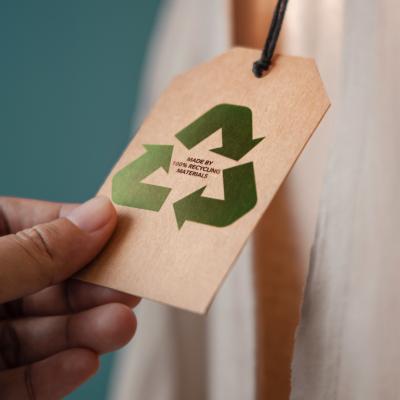 Close up of hand holding a tag that says Made By 100% Recycling Materials attached to a product.
