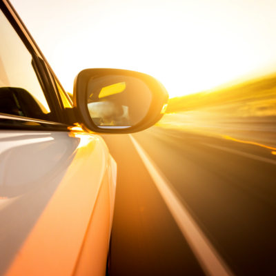 The side mirror of a white car speeding down the highway at sunset.