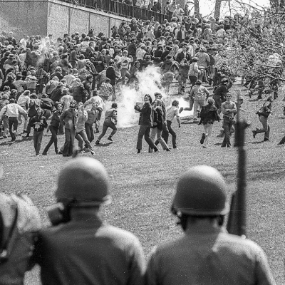 National Guardsmen in gas masks with rifles drive back Kent State University students.