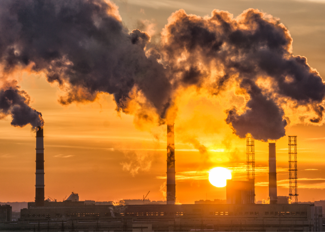 Dark gray smoke billows out of factory stacks as the sun sets. 