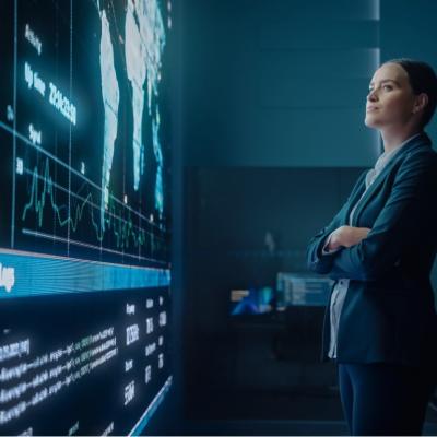 A young woman looking at big screen display showing global map with data points.