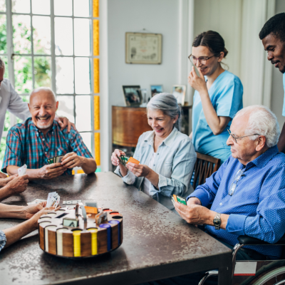 A group of older adults play games at a table with medical staff smiling behind them.