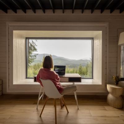 A woman working at a desk looking out on green mountains.