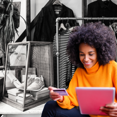A woman shopping online in front of a black-and-white image of a clothing store.
