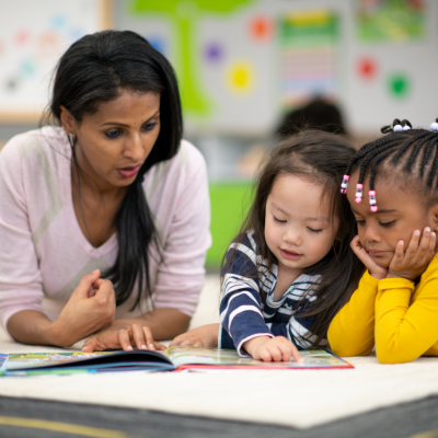 A teacher reading to two toddlers in a classroom.