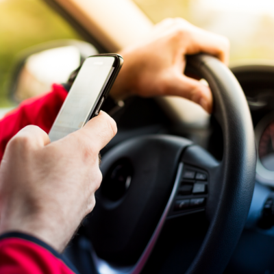 Driver with one hand on the steering wheel and one hand texting.