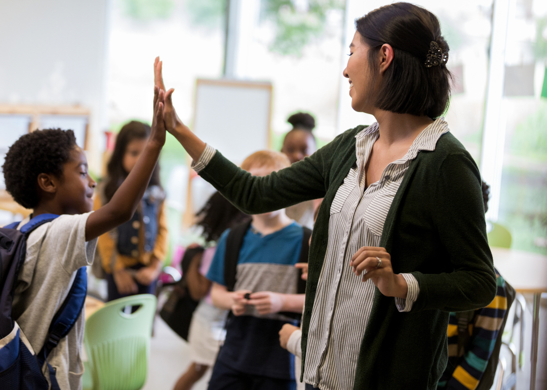 An elementary school teacher high fives a student.