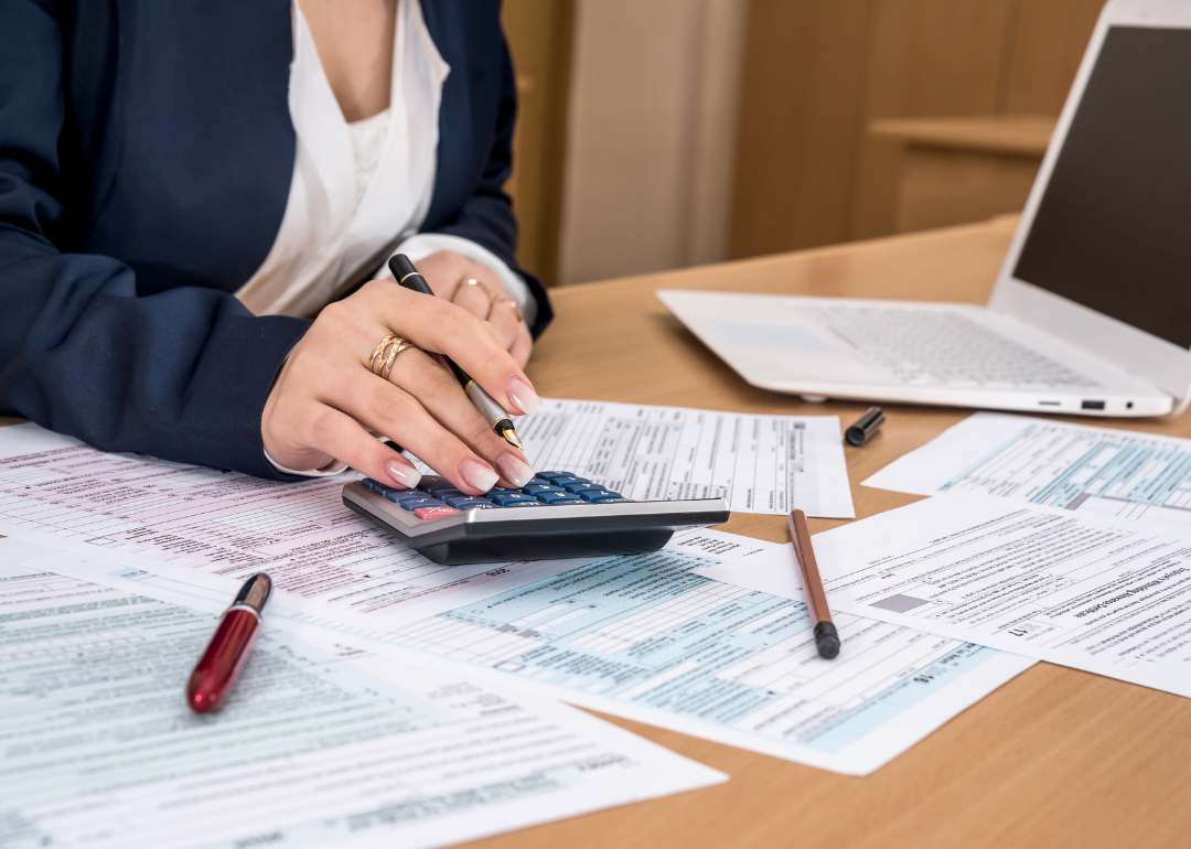 A person using a calculator to help them do their taxes while surrounded by government tax forms.