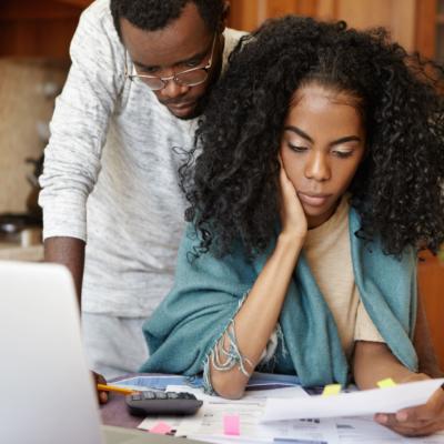 A young Black couple looking concerned while looking at their bills.