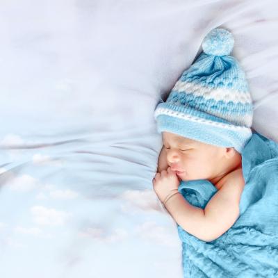 A sleeping baby bundled in a blue beanie with a pom pom and a blue blanket..