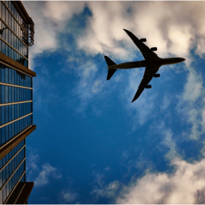 A silhouette of a airliner against blue skies, reflected in a tall building.