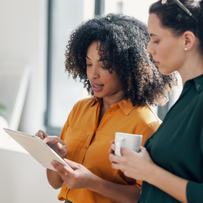 Two women look at a tablet in a bright office.