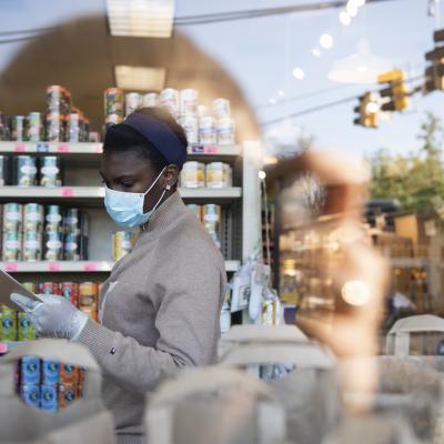 Looking through a window at a woman fulfilling a grocery pick up order at a small shop.