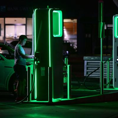 A man setting up his electric car to charge at a green lit charging station at night.