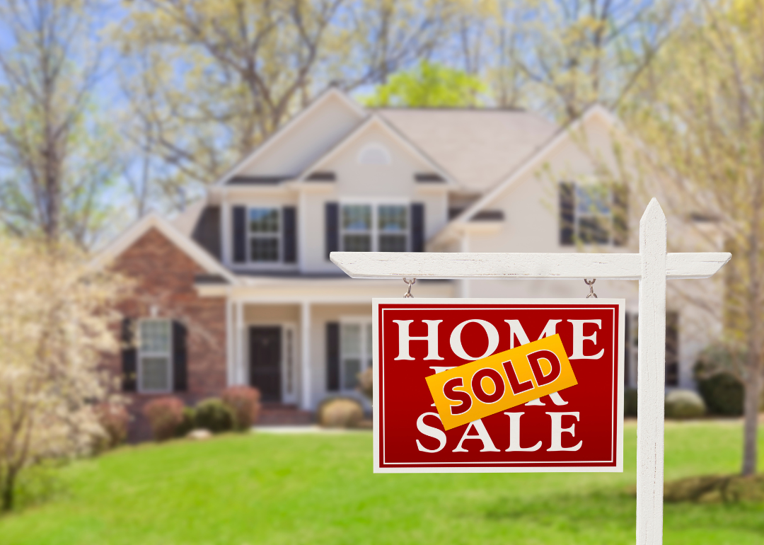 A for sale / sold sign in front of a blurred out white two-story home with black shutters. 