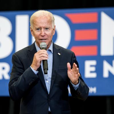 Joe Biden speaking on stage in front of a partially visible sign that reads Biden President. 
