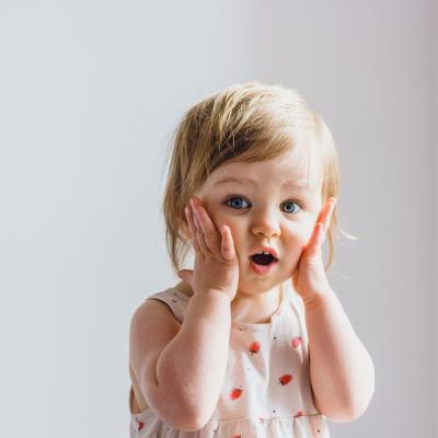 Surprised toddler with hands on her cheeks.