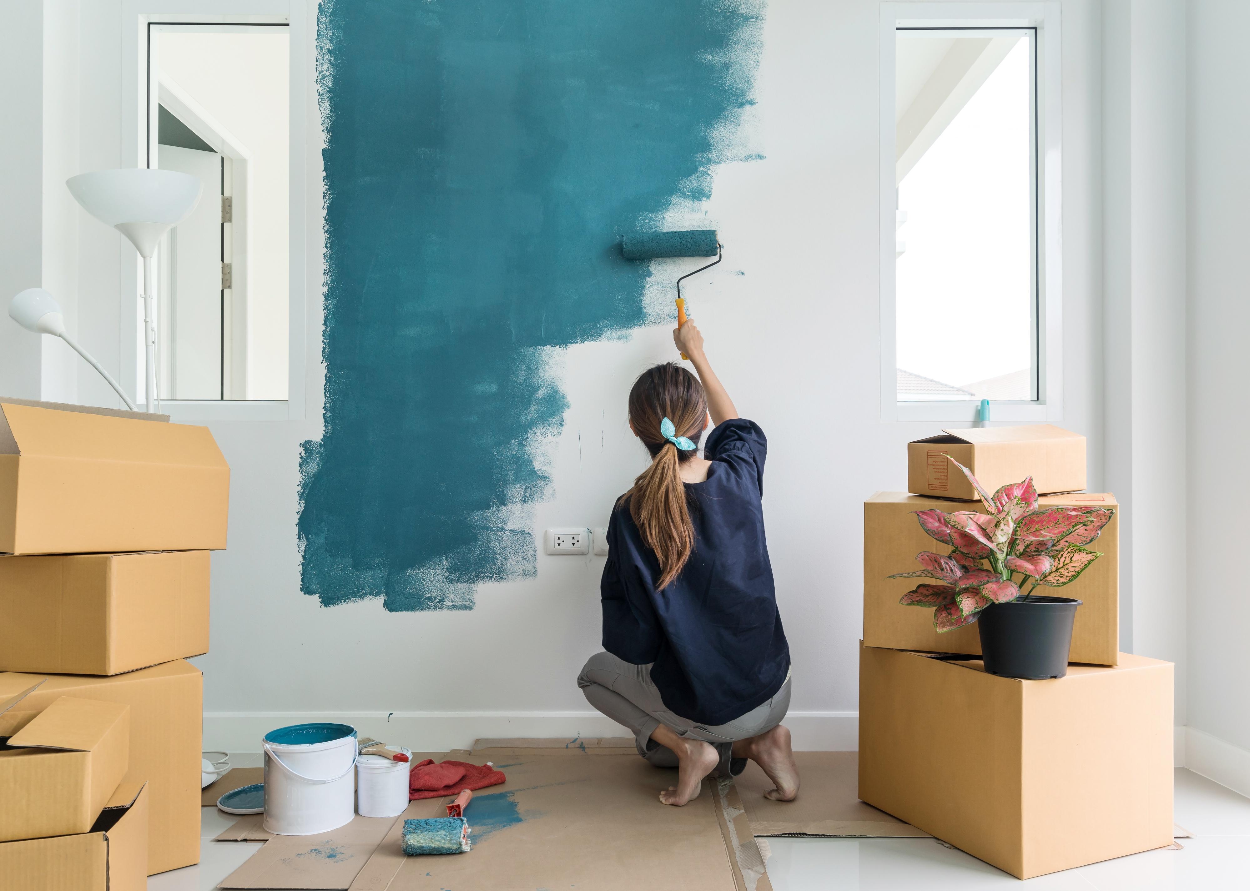 Person painting interior wall with paint roller in new house.