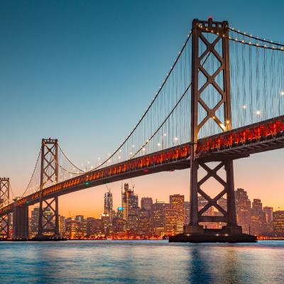 View of San Francisco skyline with famous Oakland Bay Bridge illuminated in evening light.