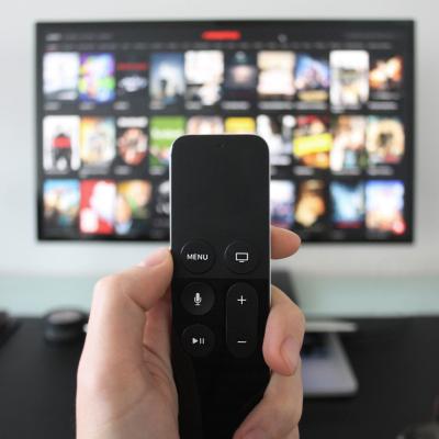Hand holding a TV remote while watching shows on a streaming service.