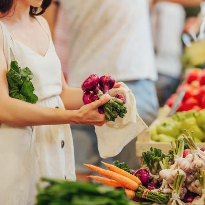 Hands putting fruits and vegetables in a cotton produce bag at food market. 