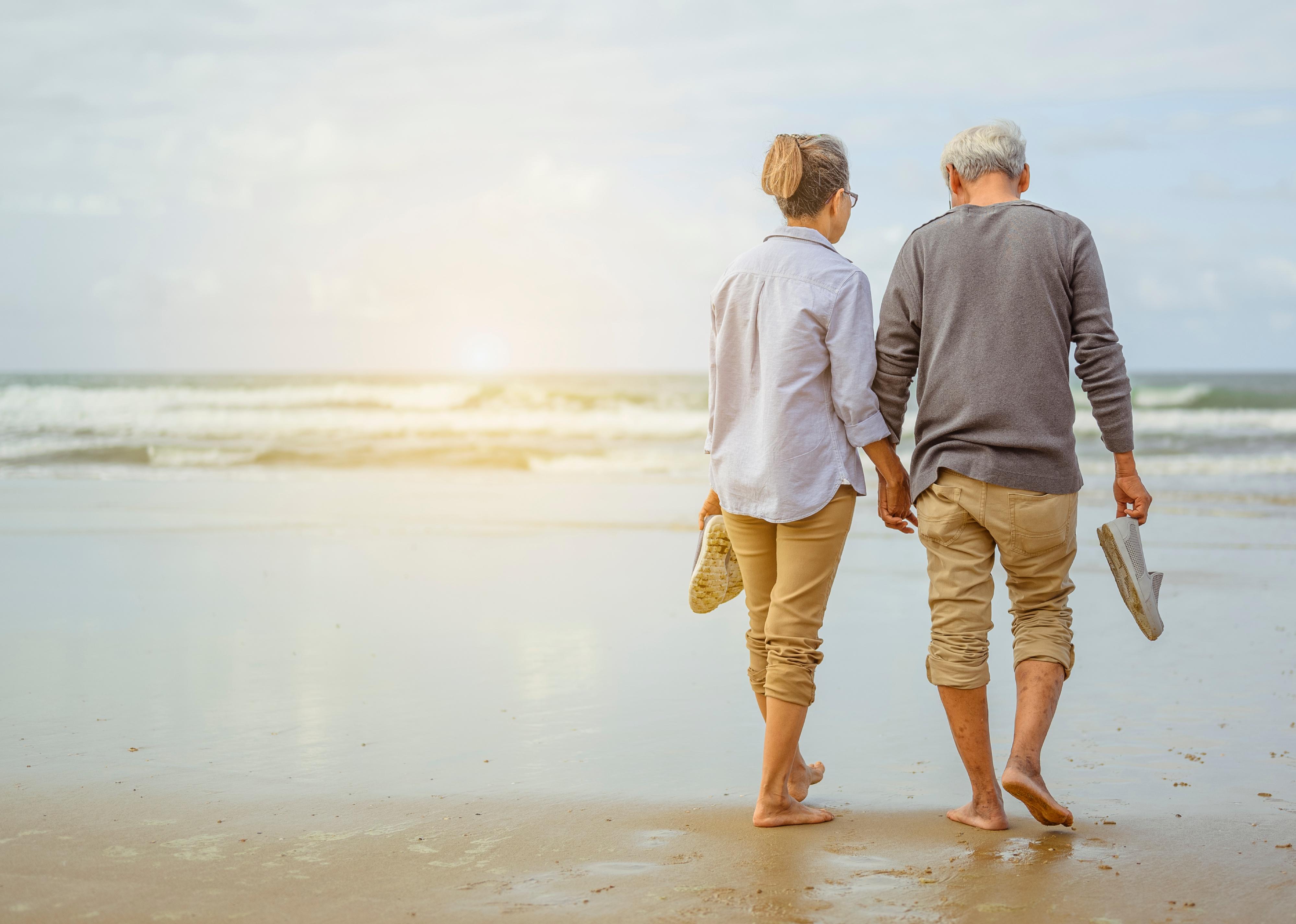 Senior couple walking on the beach holding hands.