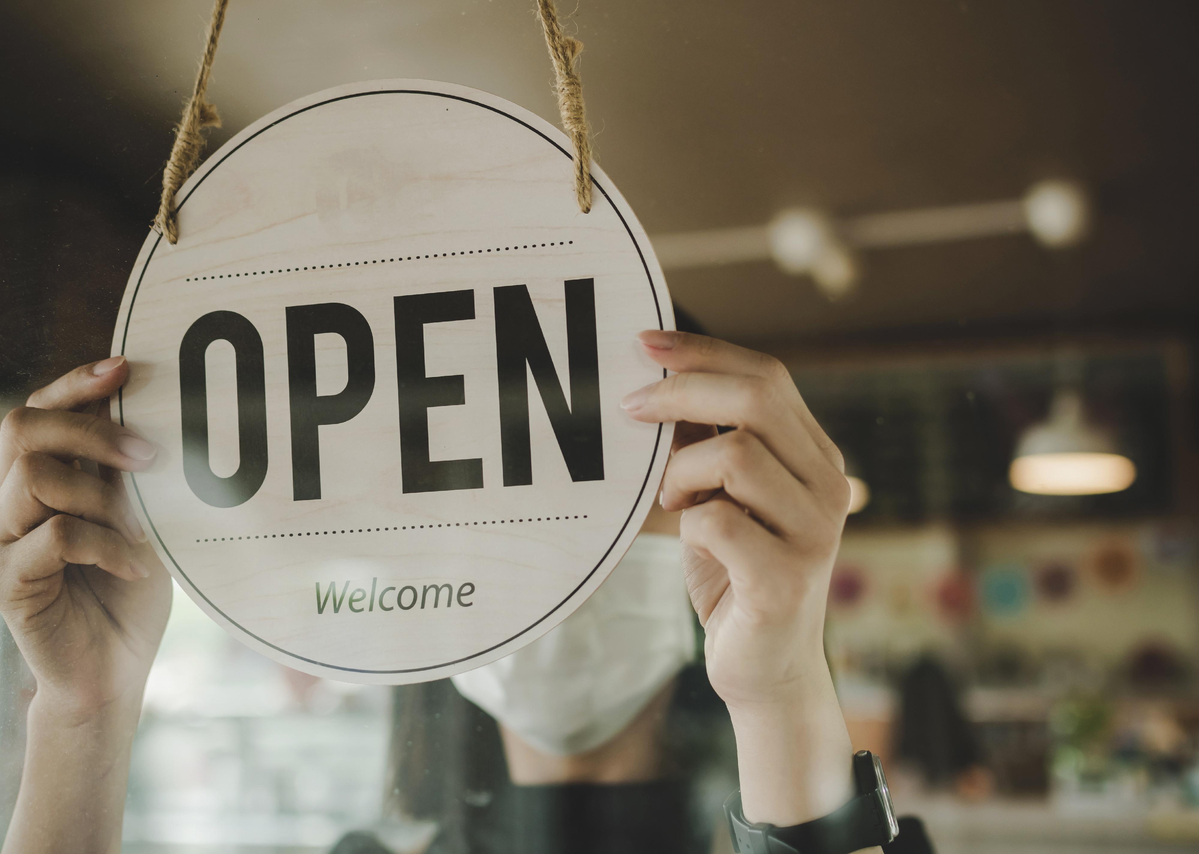 Hands turning an open sign on glass door.
