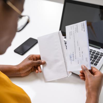 Woman holding and looking at a paycheck out of an envelope.
