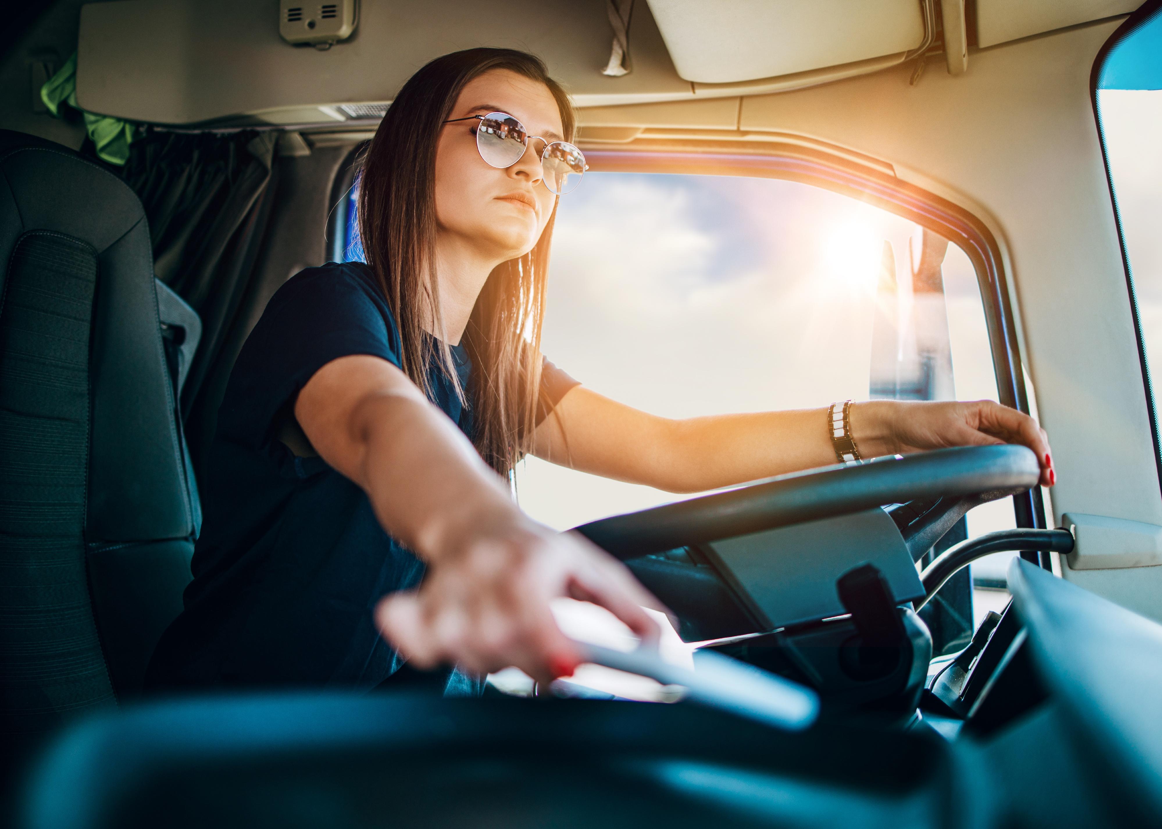 Young female professional truck driver sitting and driving truck.