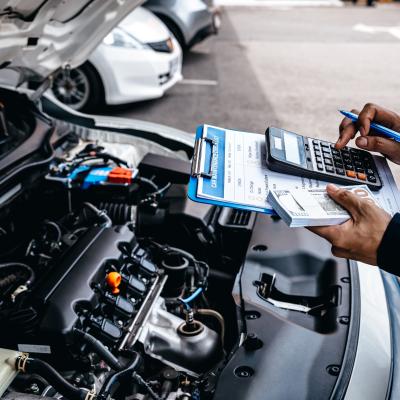 Mechanic calculates the cost of car repairs to customer at garage workshop.