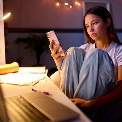 Teenage girl sitting at a desk looking at phone.