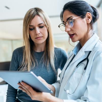 A doctor holding a tablet, speaking with a patient.