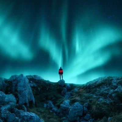 Aurora borealis and young woman on mountain peak at night.