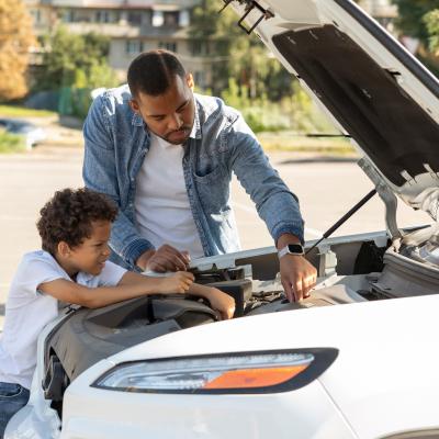 Father and son checking car engine outdoors.