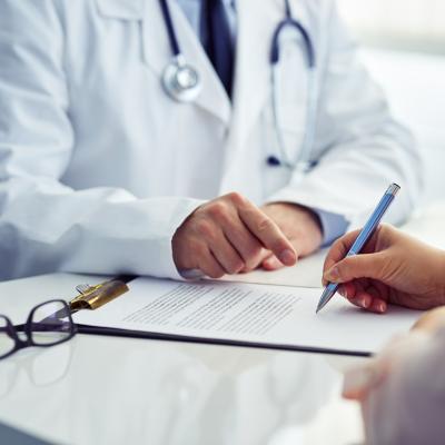 A patient in an office filling out medical document with doctor sitting across the table.