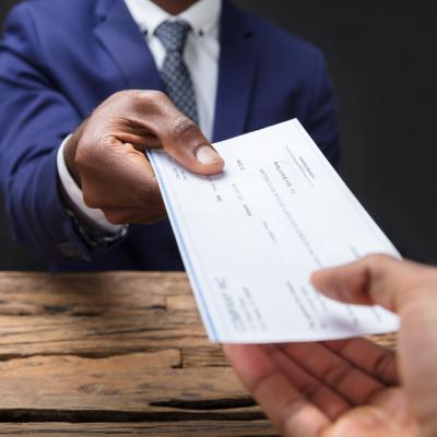 Close-up of a businessperson handing paycheck to colleague over a desk.