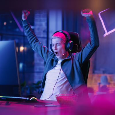 A person cheering at a computer in a dim room with neon lights.