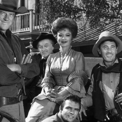 The cast of 'Gunsmoke' poses around a wagon in a promotional portrait for the Western television series. From left to right are actors James Arness, Milburn Stone, Amanda Blake, Ken Curtis, and Burt Reynholds is on the second row.