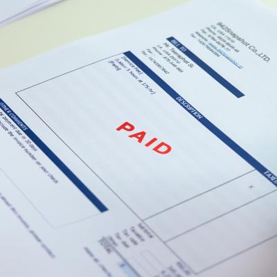Worker sealing "paid" sign on an invoice document.