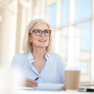 Blond professional sitting at table with large windows in the background talking in meeting.